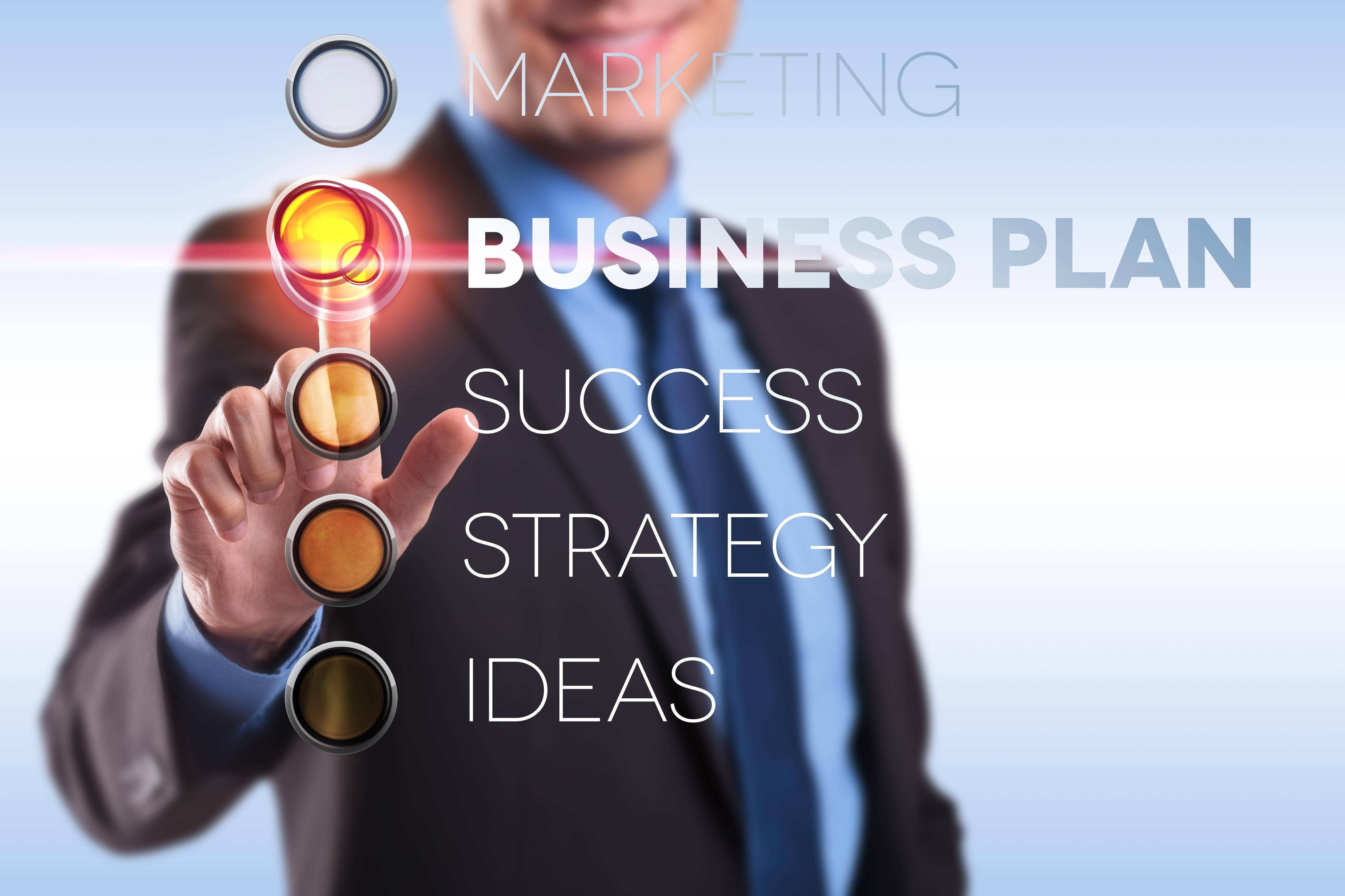 商業計劃流程 壁紙 — 一位商人按下一個發光的按鈕，上面標有 'BUSINESS PLAN'，在一個帶有浮動文字關鍵詞的未來感界面上。