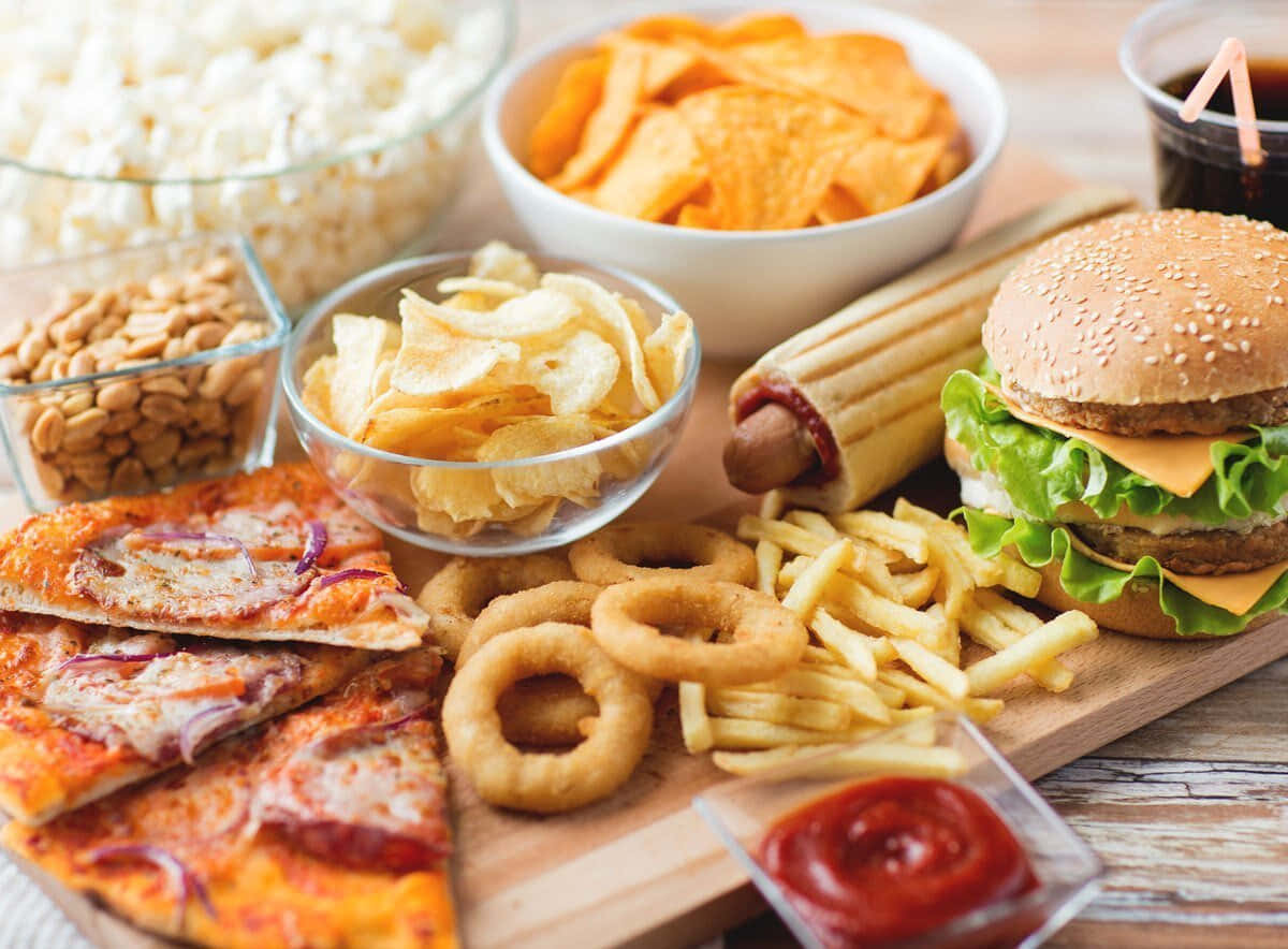 商業食品 壁紙 — 一個木板上堆滿了經典垃圾食品，包括漢堡、薯條、洋蔥圈和爆米花。
