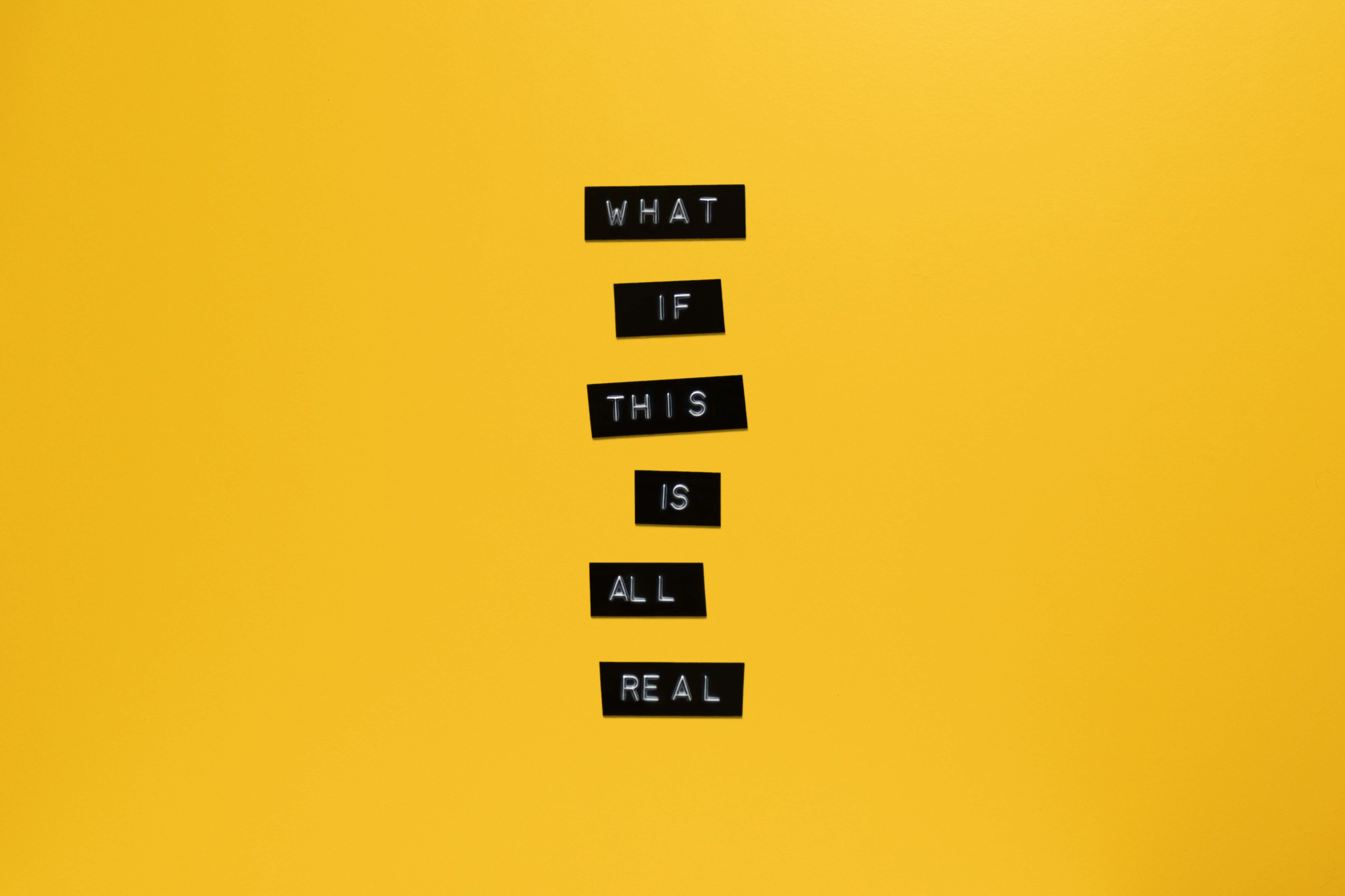 問字藝術背景 壁紙 — 黑色字母瓷磚拼出「WHAT IF THIS IS ALL REAL」，垂直立在鮮黃色背景上。