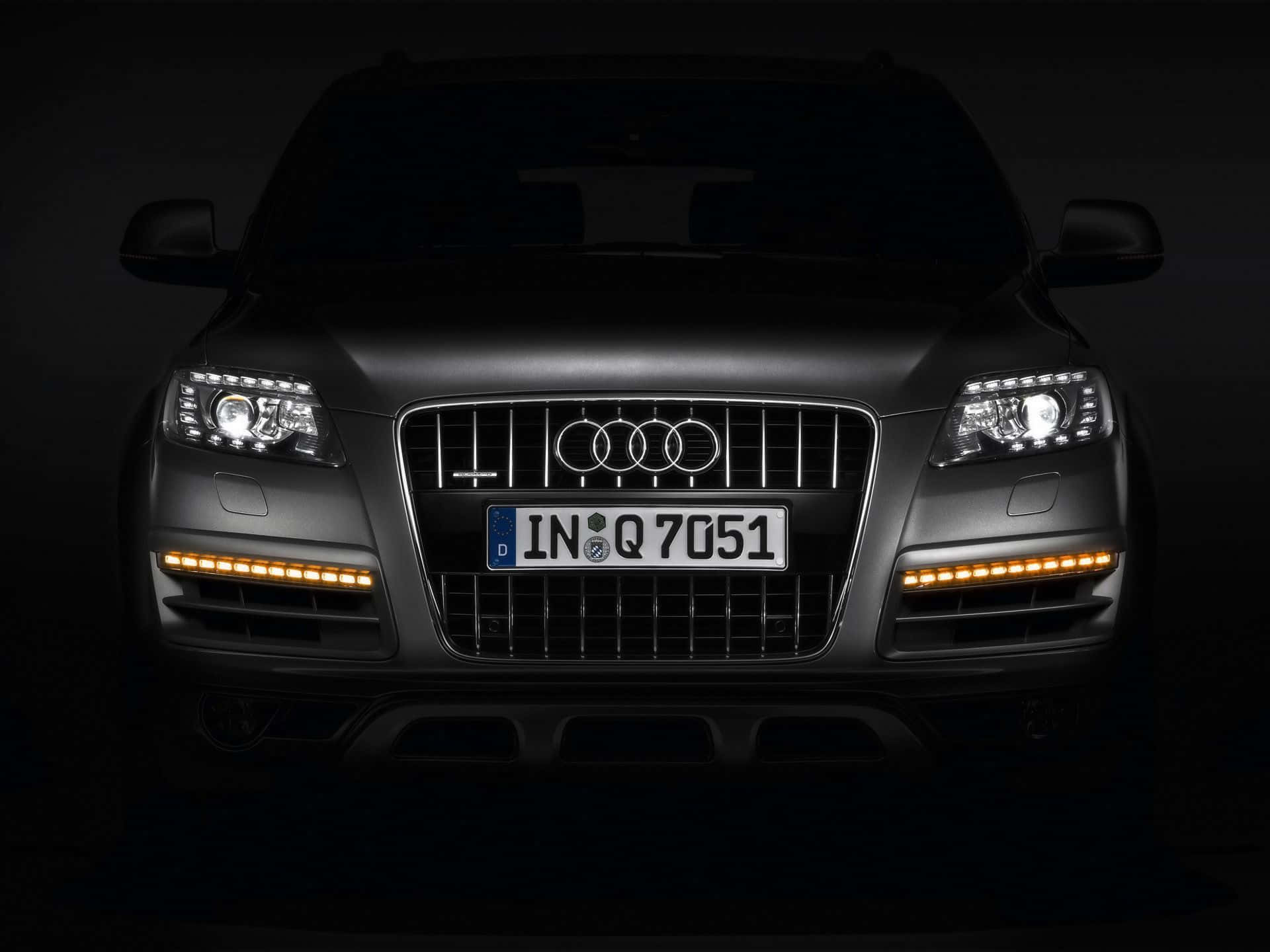 Audi Q7 桌布 壁紙 — 啞光黑色奧迪Q7 SUV的前視圖，由發光的頭燈和日間行車燈照亮，背景為深色。