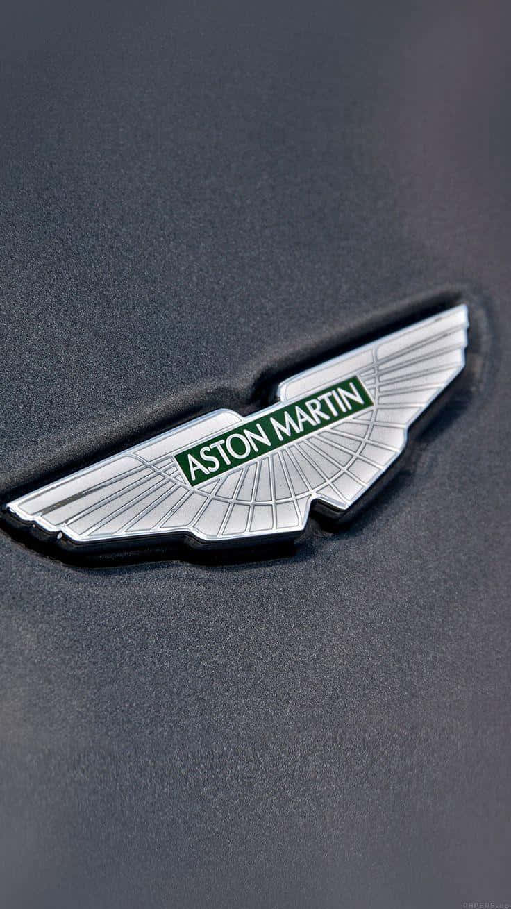 Car Logo 桌布 壁紙 — 啞光黑色車身上帶有綠色文字的閃亮銀色Aston Martin翼形標誌特寫。