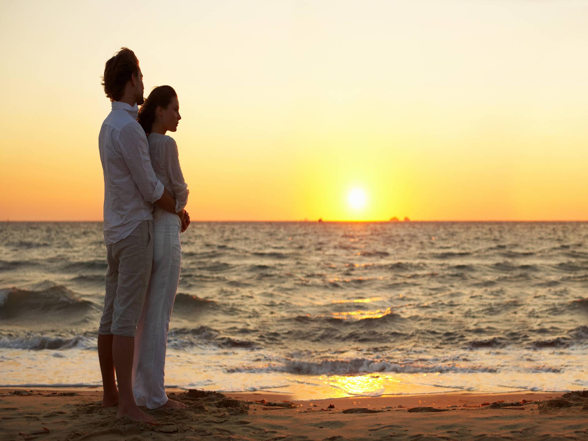 一對情侶站在沙灘上，看著夕陽在海面上落下。