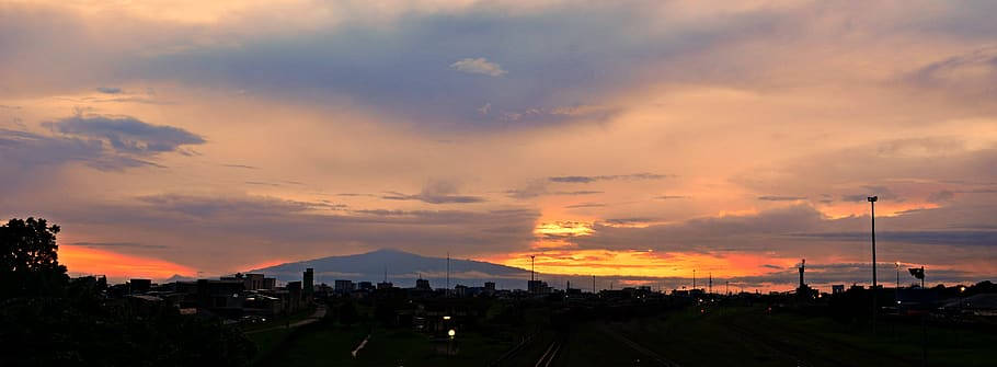 城市天際線在鮮豔的夕陽下呈現剪影，遠方有山。