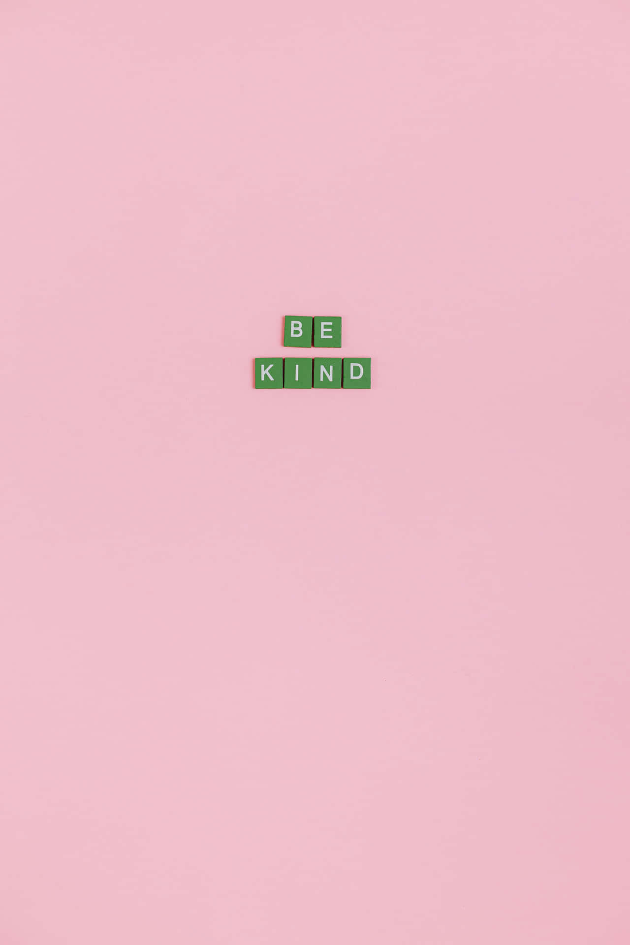 在粉紅色背景上，綠色拼字磚拼出「Be Kind」。