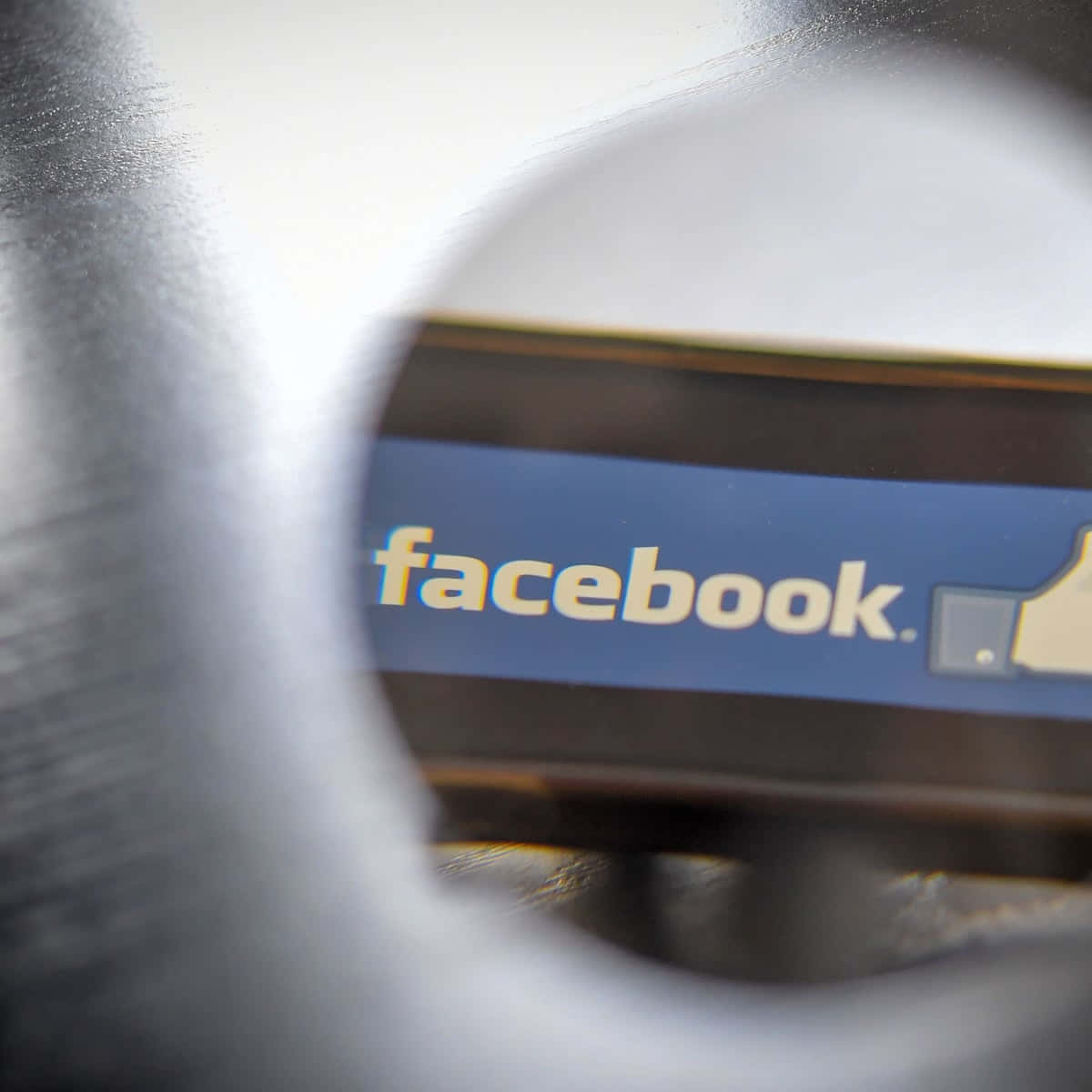 透過圓形開口看到的Facebook標誌，金屬邊緣模糊。