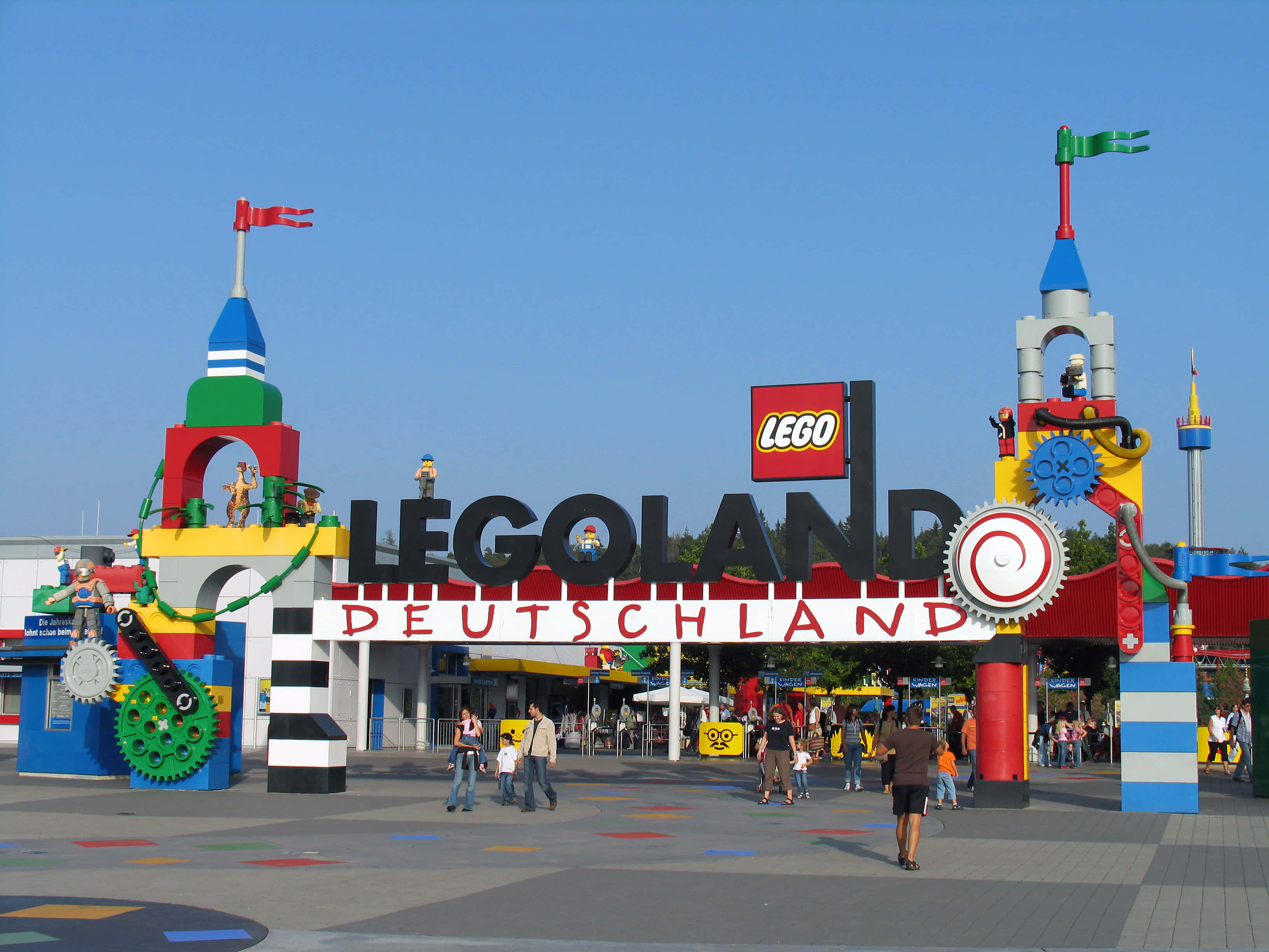 喚醒你的想像力，來樂高樂園 壁紙 — 色彩繽紛的LEGO主題入口，通往LEGOLAND Deutschland，擁有彩色積木塔、齒輪和遊客，在晴朗藍天下。
