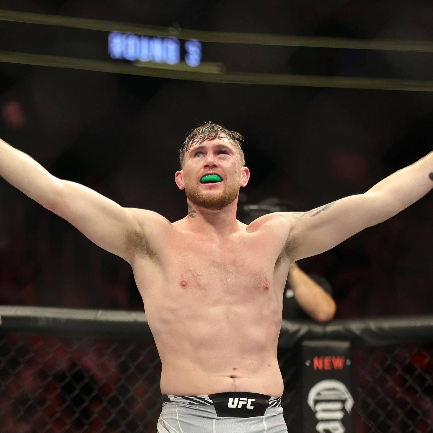 喜悅的達倫·蒂爾 壁紙 — 一位勝利的UFC拳手在八角籠內高舉雙臂慶祝，戴著綠色護齒。