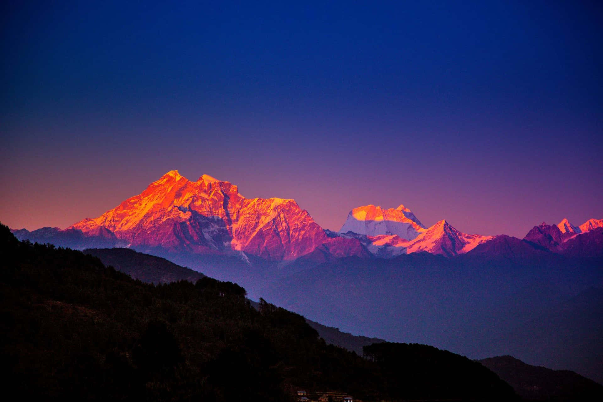 白雪覆蓋的山脈沐浴在橙色夕陽光中，位於黑暗森林山丘之上。