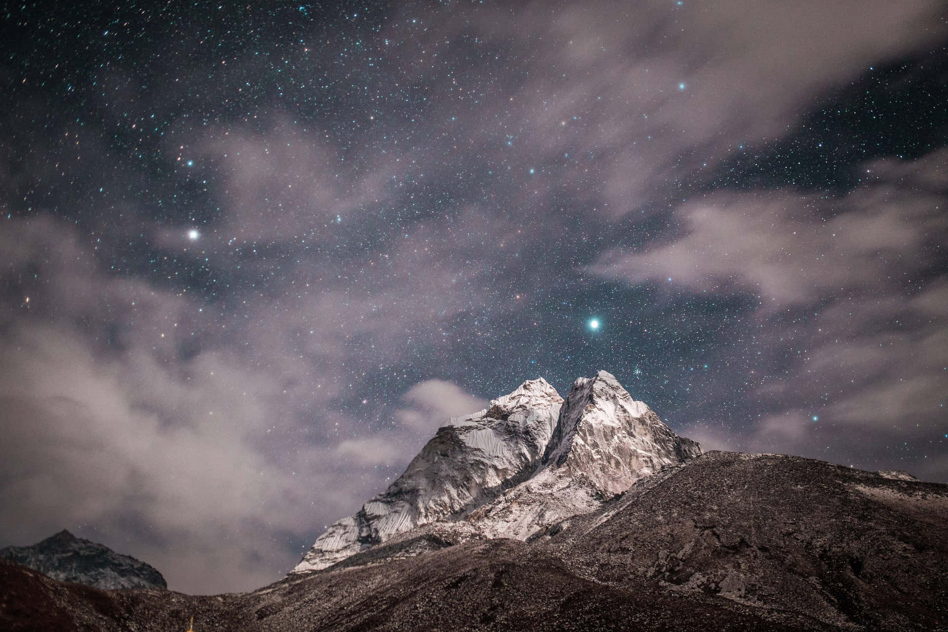 白雪覆蓋的山峰，繁星點點的夜空下，飄動的雲朵和一顆可見的彗星。