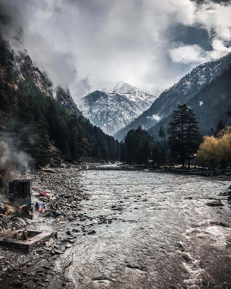 一條河流蜿蜒穿過積雪的山谷，有常綠樹木和霧氣。