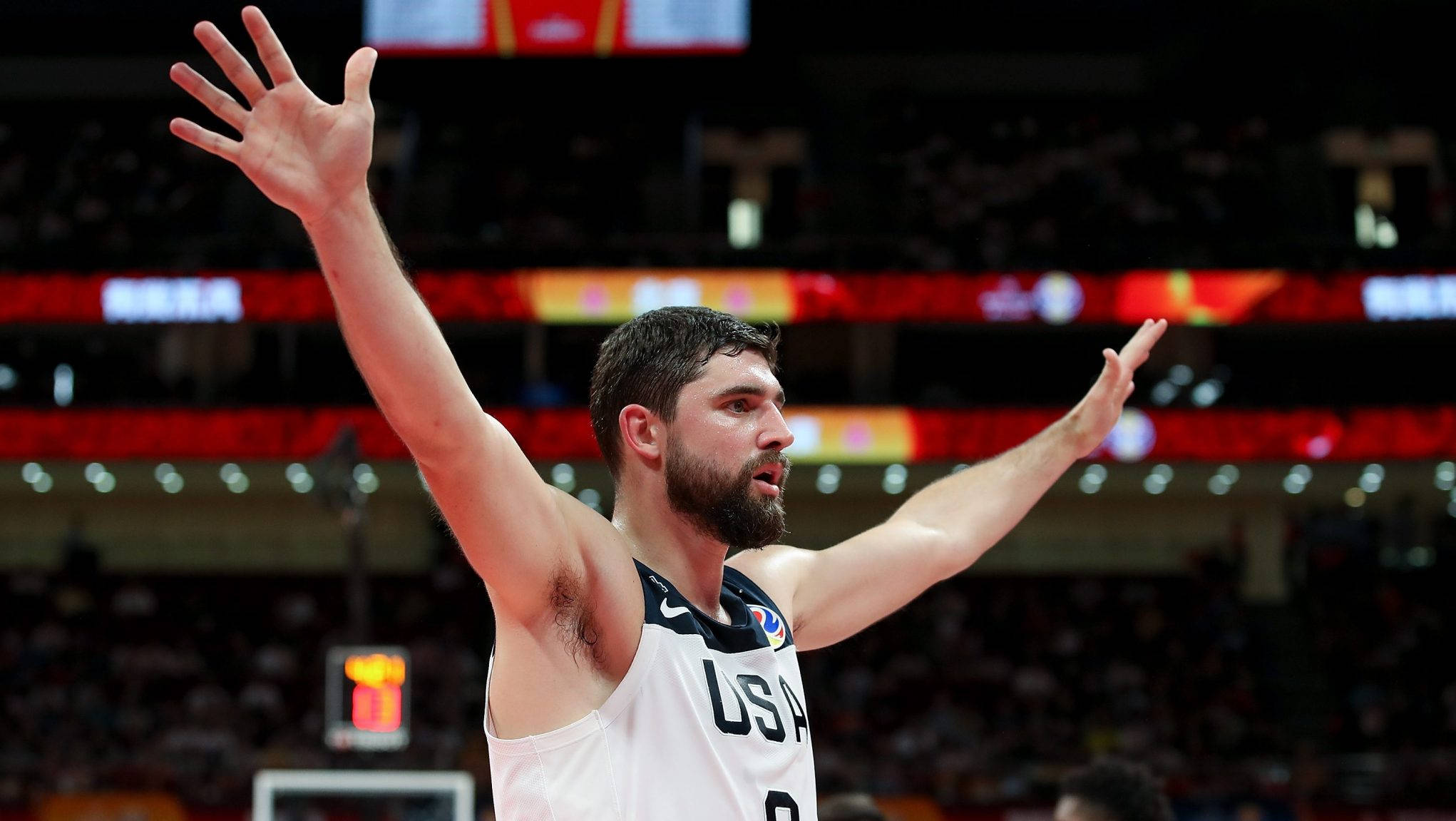 喬·哈里斯 2019 年 FIBA 壁紙 — 一名美國籃球運動員在燈光明亮的球場上高舉雙臂慶祝勝利，面前是歡呼的人群。