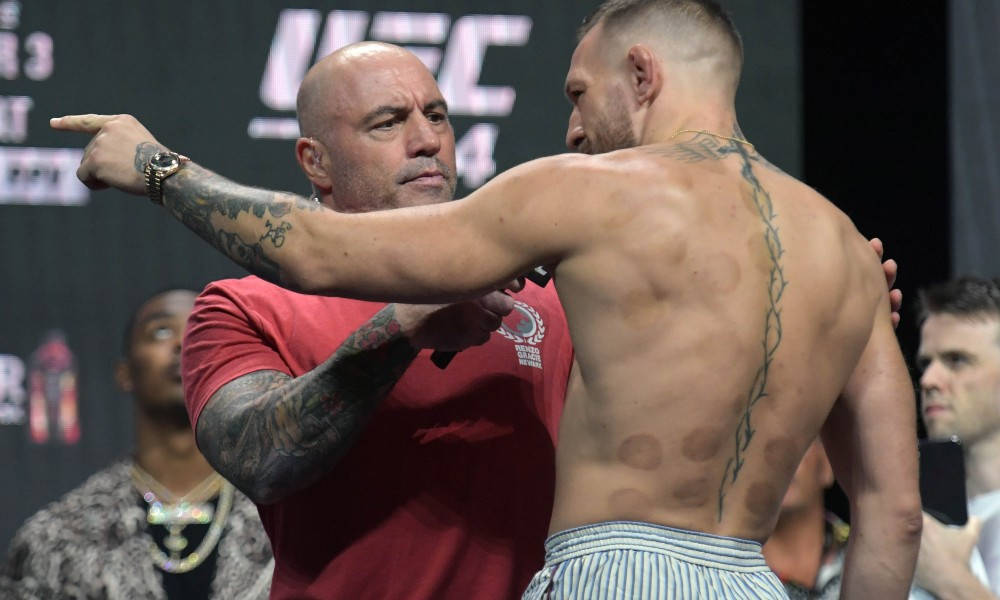 UFC戰士背上有紋身和拔罐印記，被一位身穿紅衫的光頭男子引導。