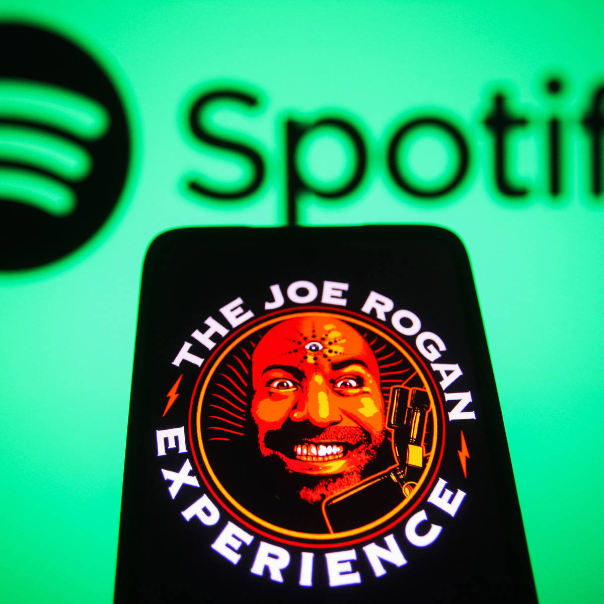 智能手機顯示Joe Rogan Experience播客標誌，背景有Spotify標誌。