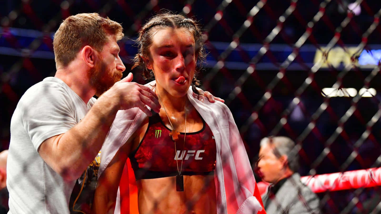 一位瘀傷的女性MMA拳手在比賽後於籠中被一名男子安慰。