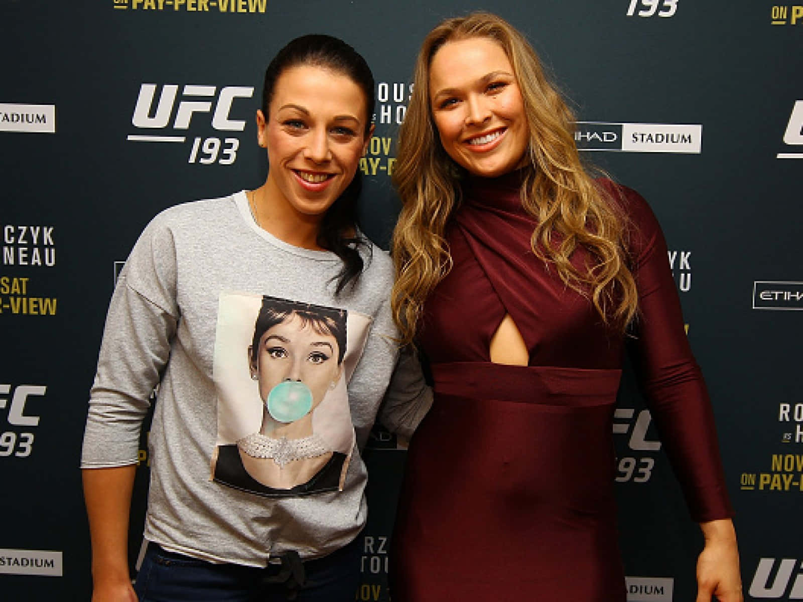 兩位女性在UFC活動中，一位穿著休閒T恤，另一位穿著優雅連衣裙，兩人都微笑。