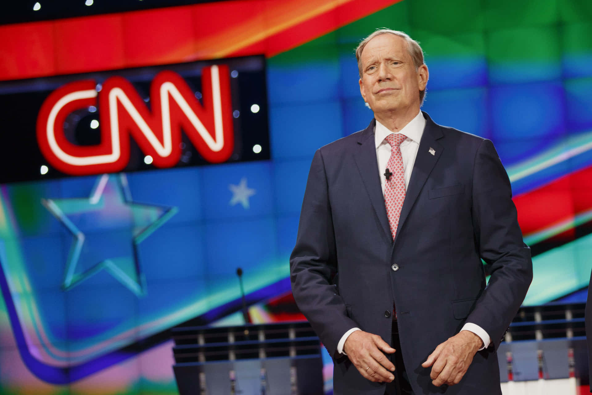 男子身穿西裝站在CNN新聞工作室，背景色彩繽紛。