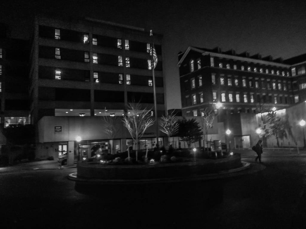 夜景城市景觀，有亮燈的窗戶和一個人在花盆附近行走。
