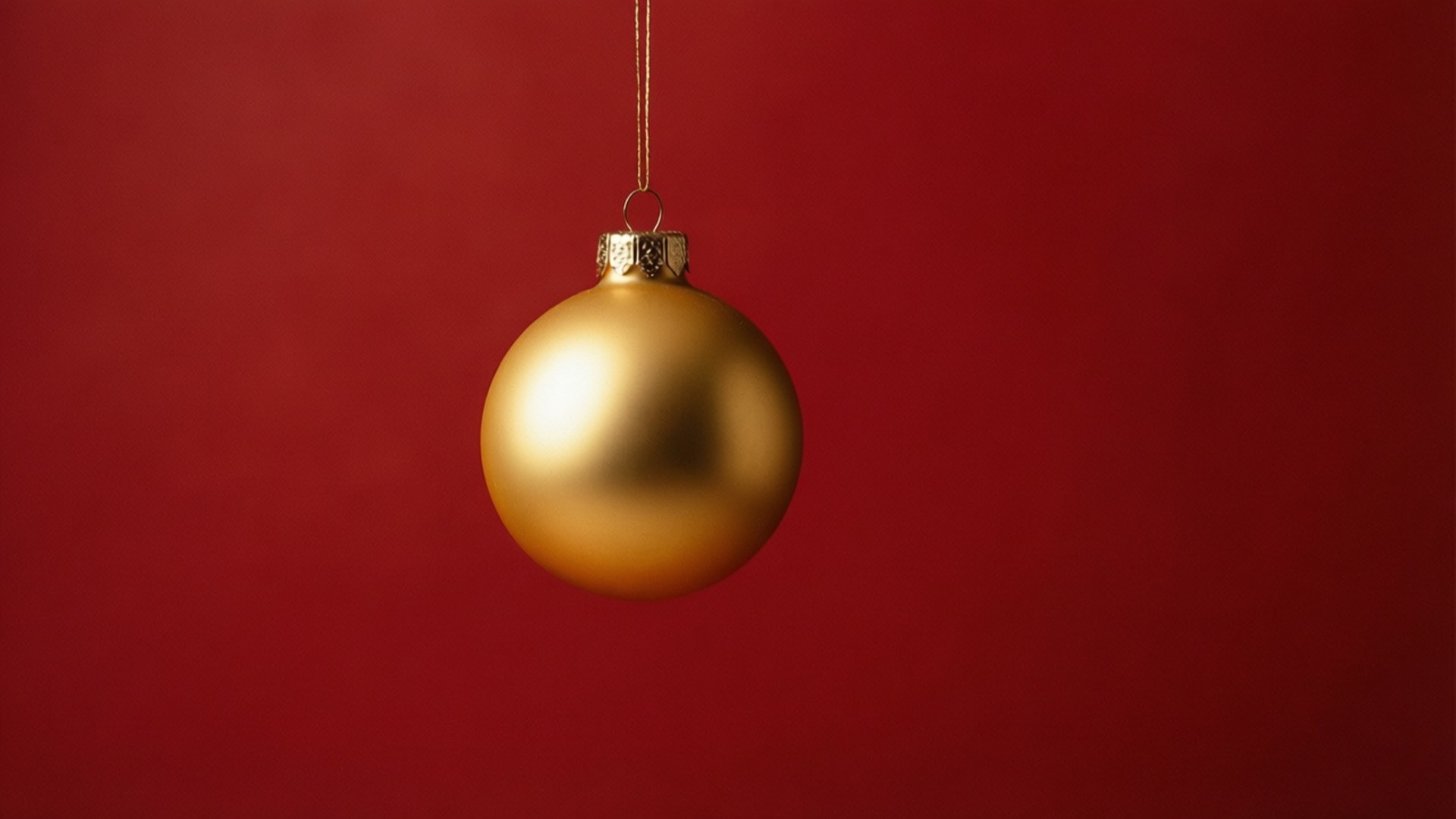 單一金色裝飾 壁紙 — 一個啞光金色聖誕裝飾品用細繩掛在純深紅色背景上。