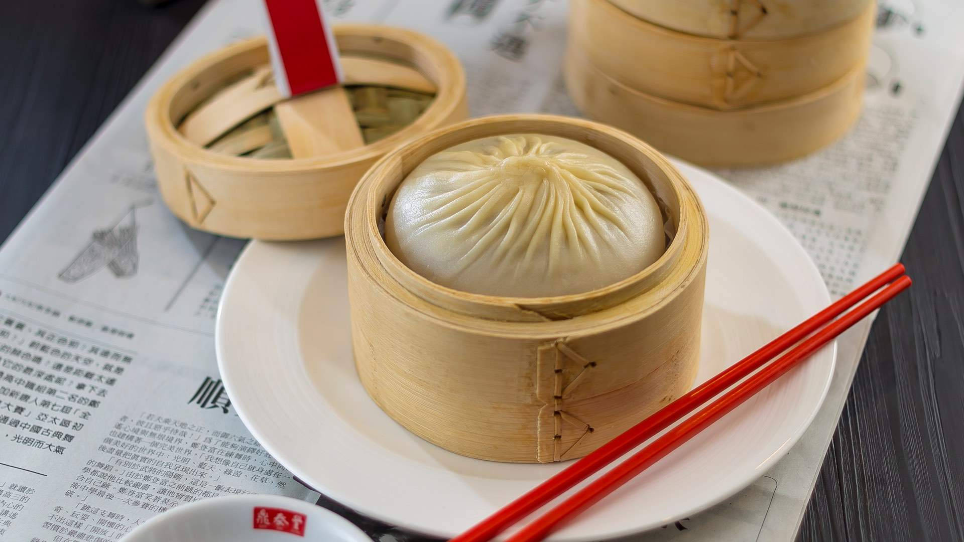 竹蒸籠裡的蒸餃，配紅色筷子，放在報紙上。
