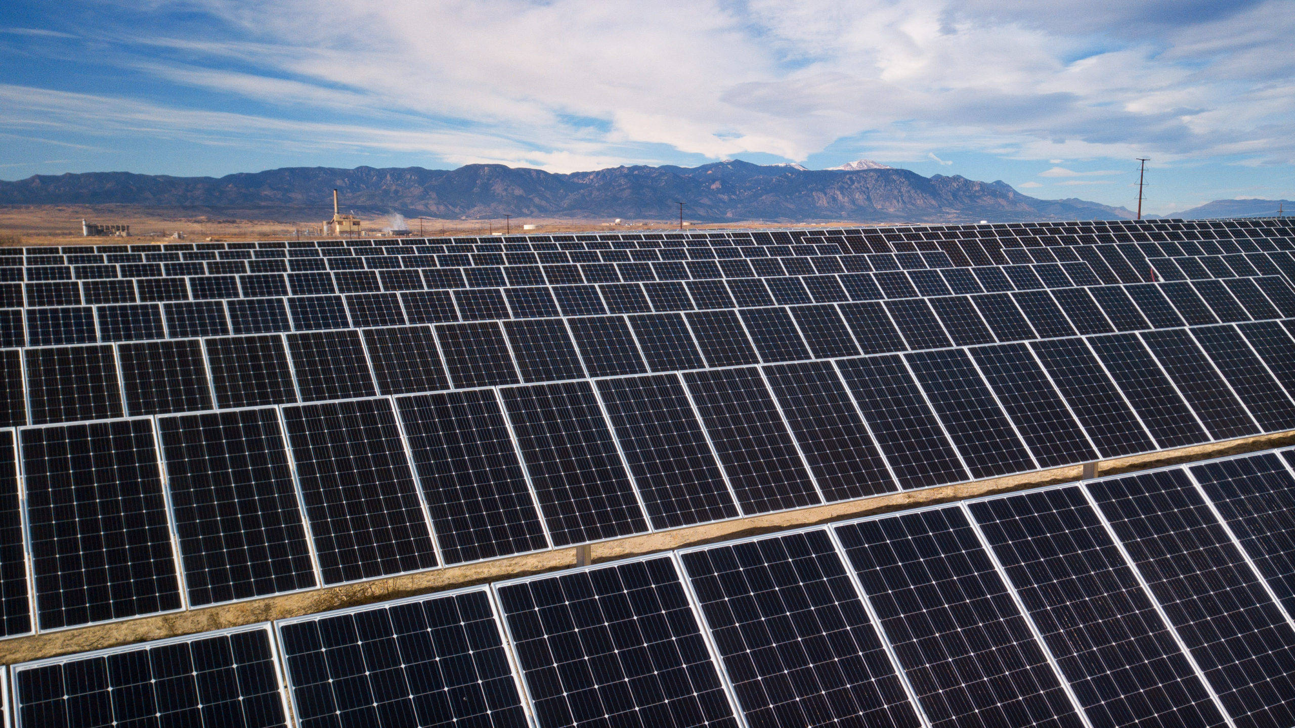 單晶NV Energy太陽能板 壁紙 — 一排排太陽能板在藍天下延伸穿過沙漠景觀，遠處有積雪覆蓋的山脈。