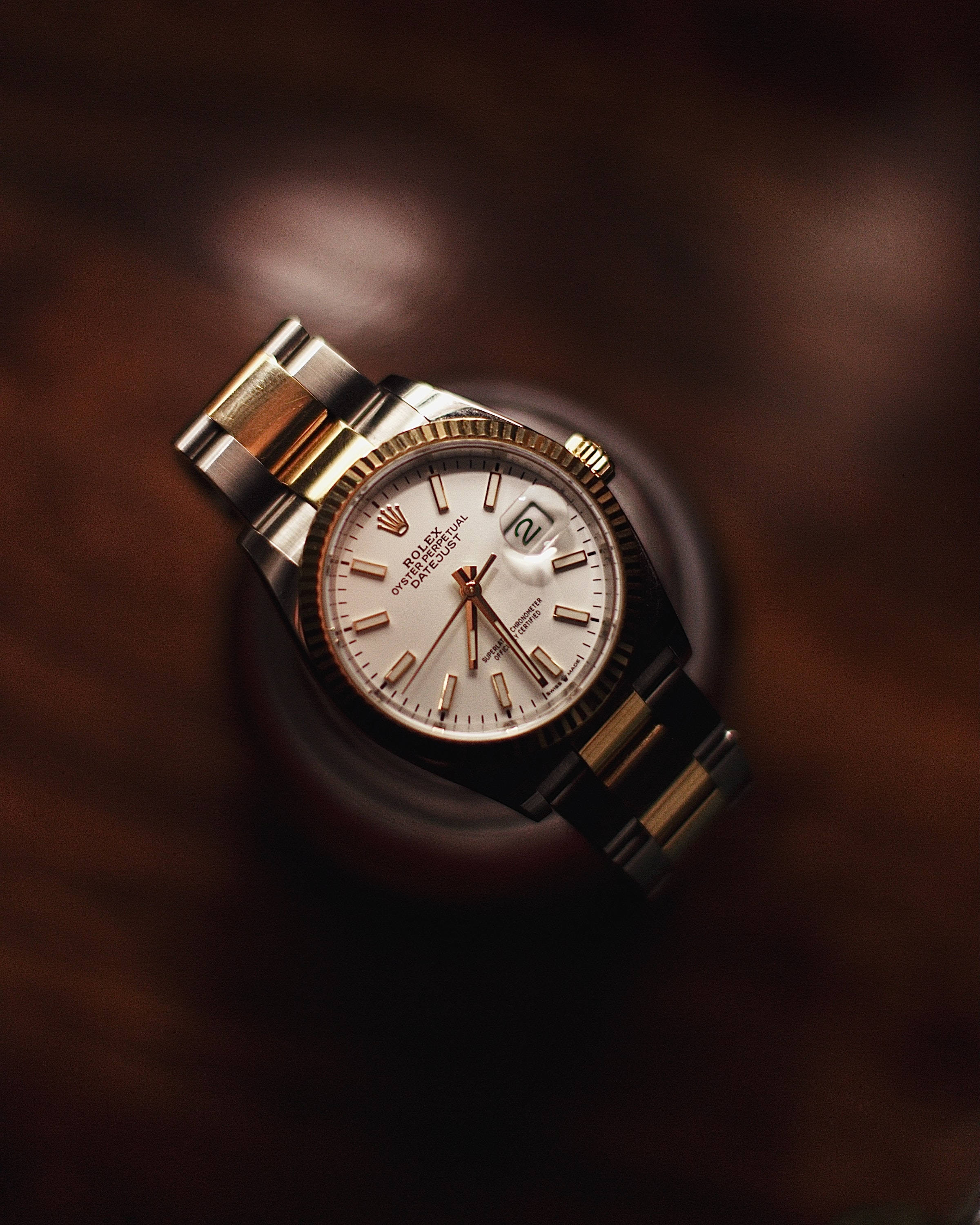 單獨羅夏錶特寫 壁紙 — 一隻豪華的金色和鋼色勞力士Oyster Perpetual Datejust手錶放在豐富的棕色木質表面上，帶有柔和溫暖的燈光。