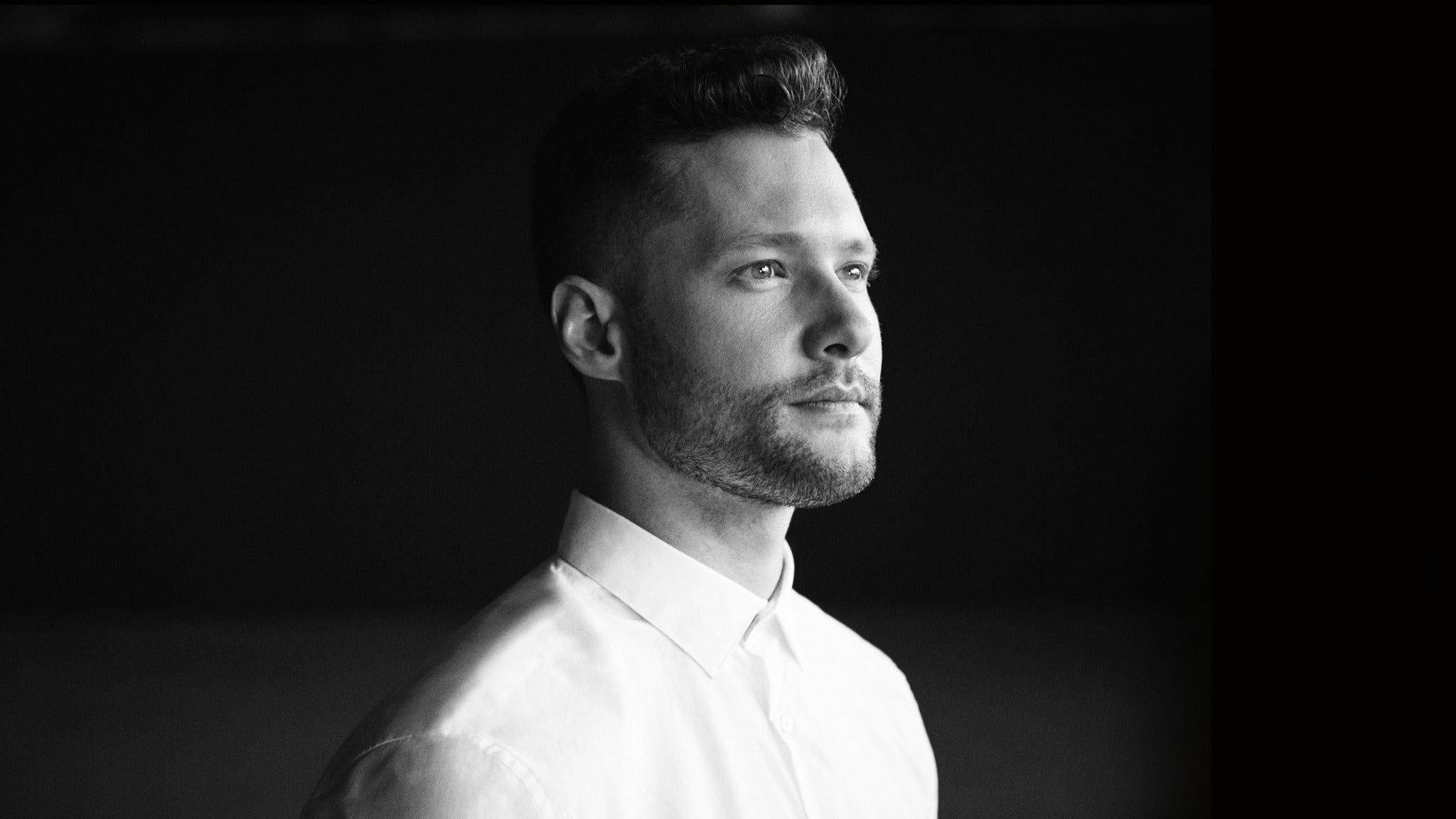 單色 Calum Scott 壁紙 — 一個穿著白恤衫的男人在深色背景下沉思凝視的黑白肖像。
