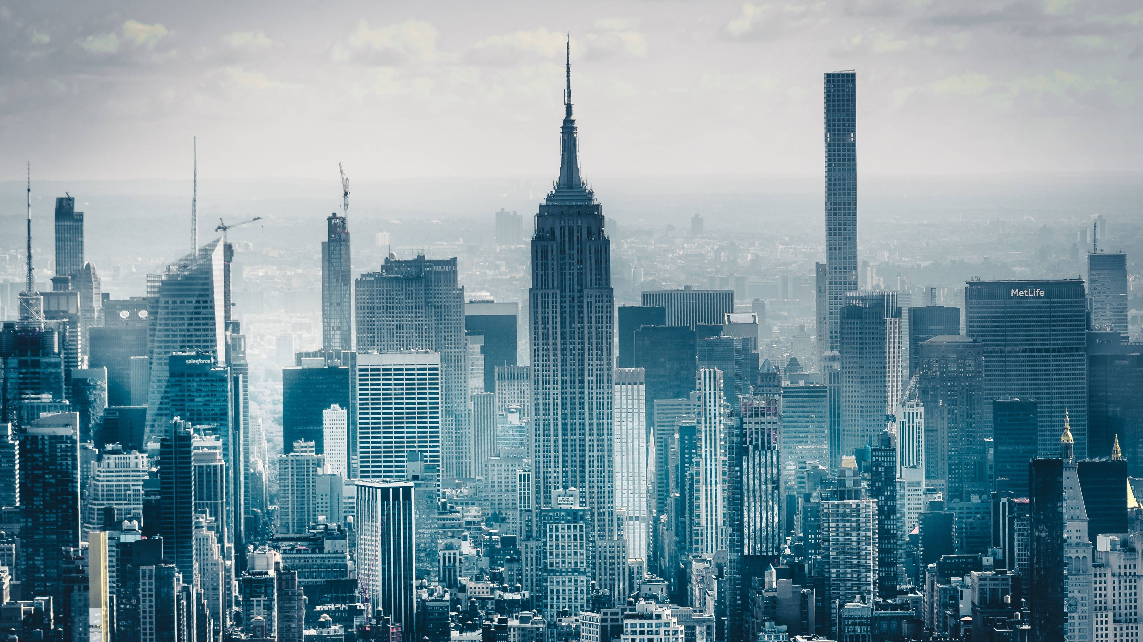 單色4K紐約市景 壁紙 — 紐約市天際線的朦朧藍色全景，以帝國大廈和現代摩天大樓為主，天空多雲。