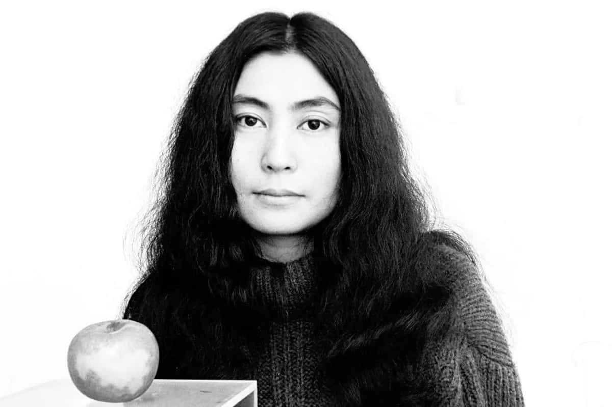長黑髮女性與桌上蘋果的黑白工作室肖像。