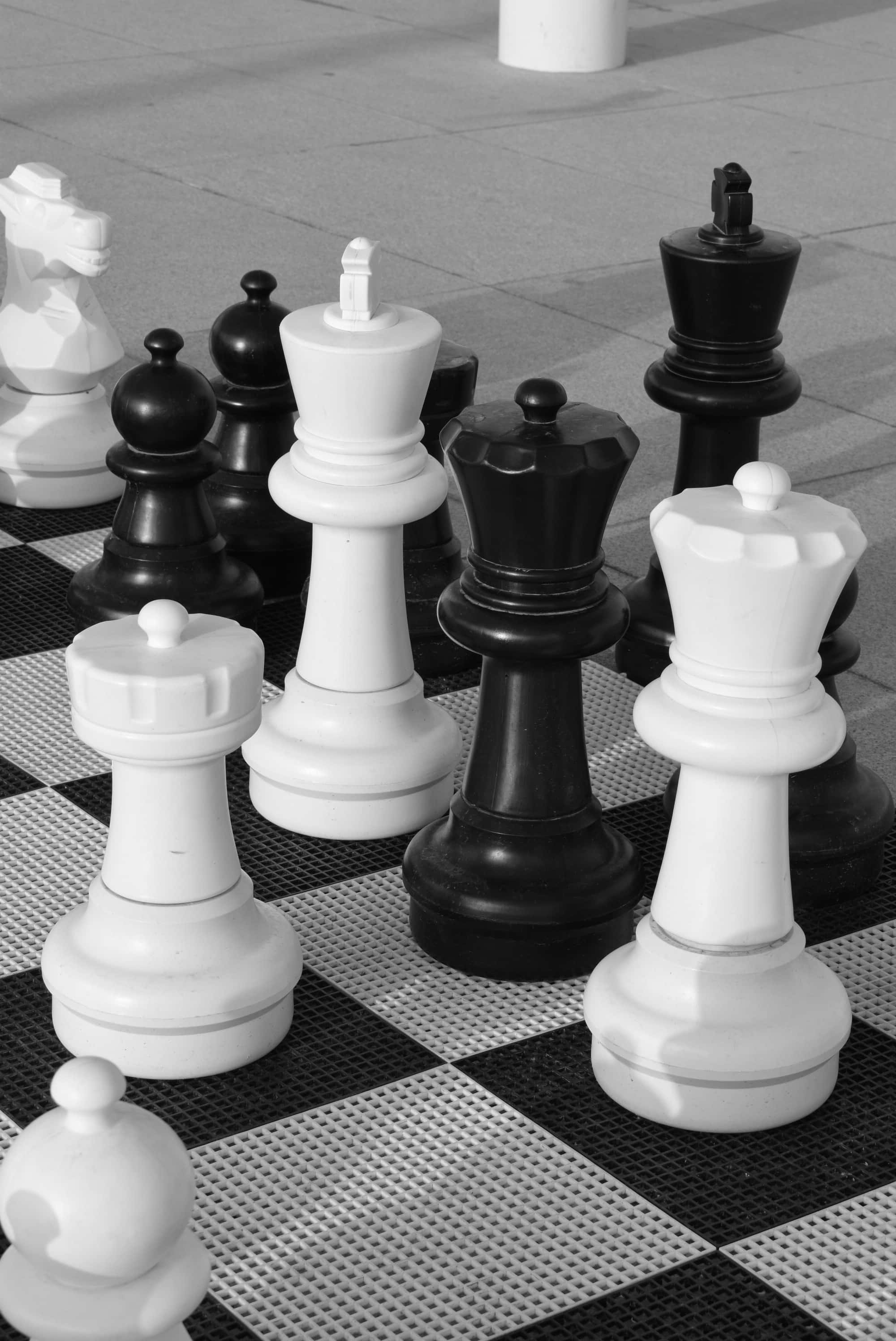 Black And White Chess 桌布 壁紙 — 單色巨型國際象棋棋子矗立在戶外棋盤上，在人行道上投下銳利的陰影。