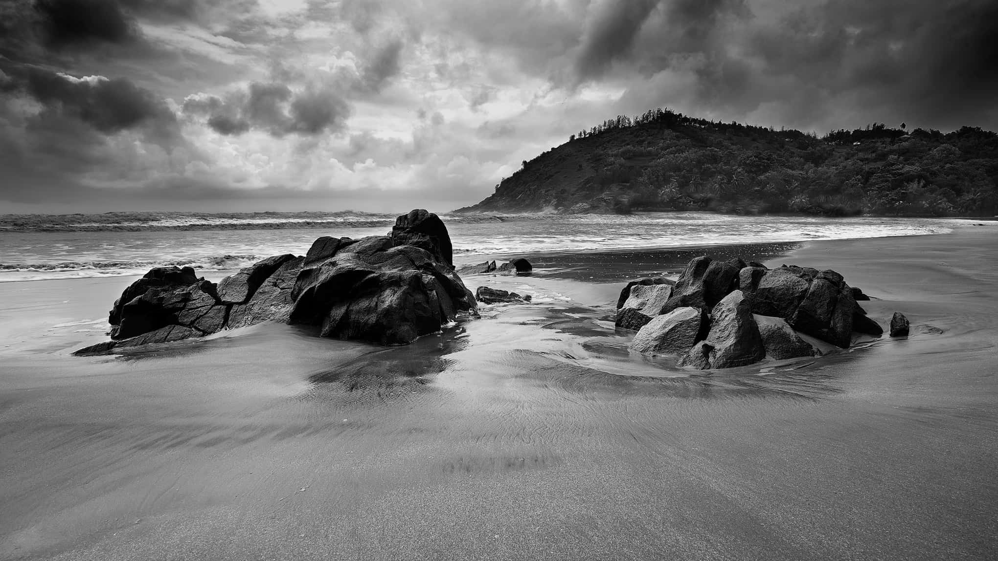 Beach Photography 桌布 壁紙 — 單色海灘場景，戲劇性的暴風雲籠罩著崎嶇的岩石和拍岸的浪花。