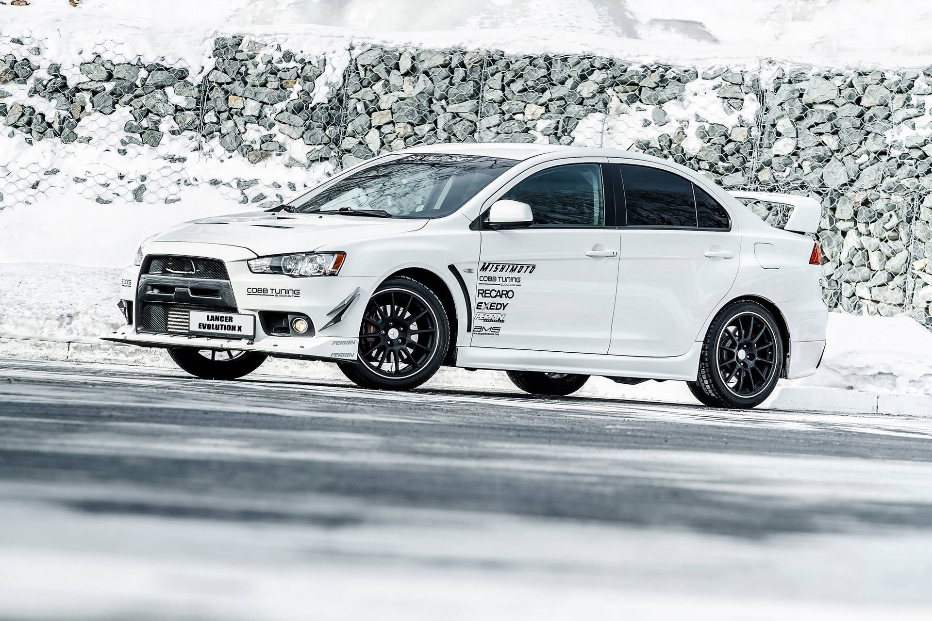 白色三菱Lancer Evolution X在雪路上靠近石牆飄移。