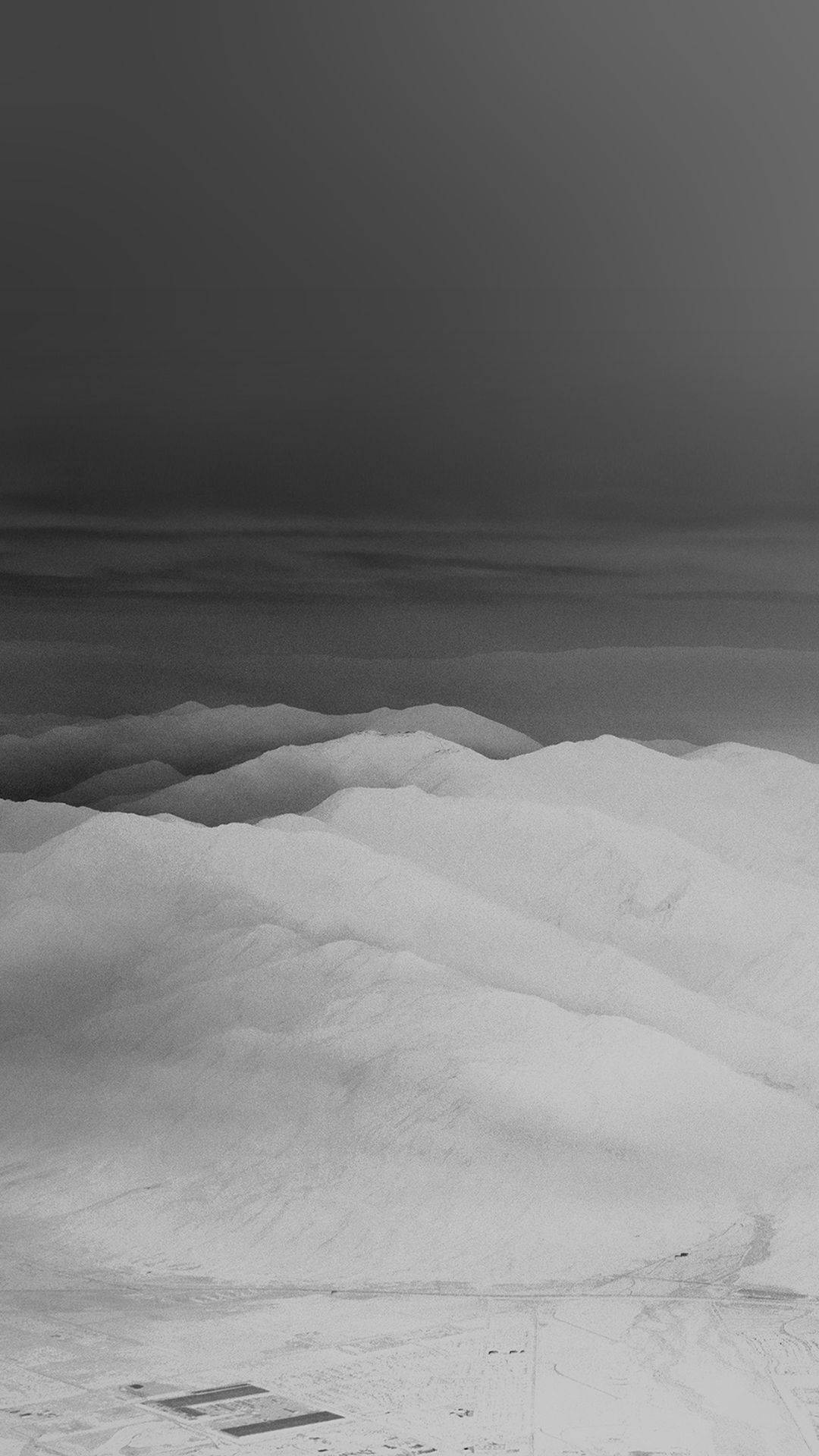 View 桌布 壁紙 — 單色航拍視圖，雪覆蓋的山脊在陰暗多雲的天空下，帶有微妙的雲層。