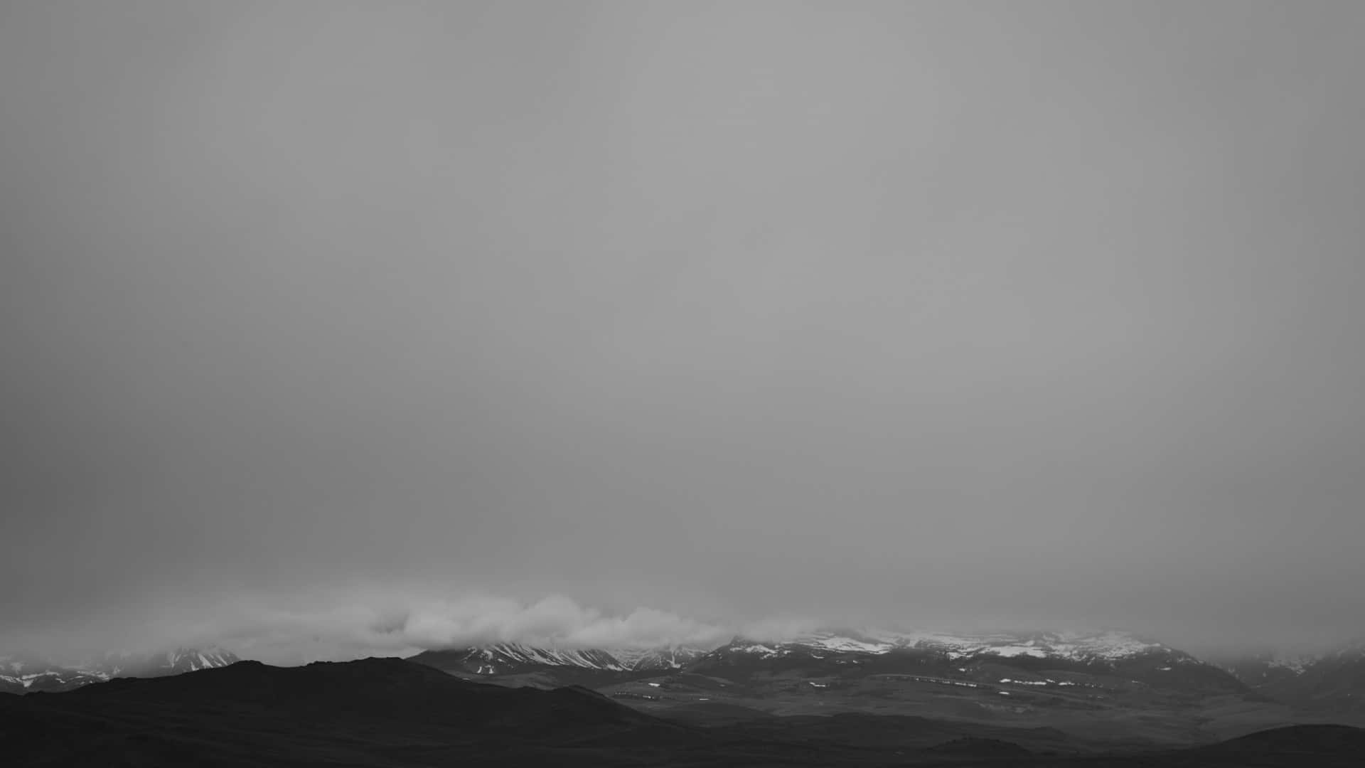 黑白美學 桌布 壁紙 — 單色調山脈，積雪的山峰在陰天低垂的雲層中若隱若現。