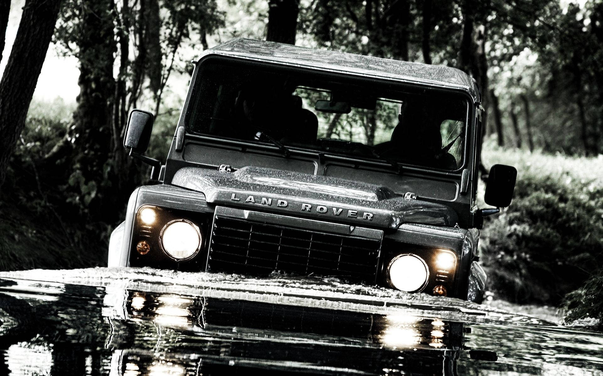 黃昏時分，一輛 Land Rover Defender 涉水穿過森林溪流。