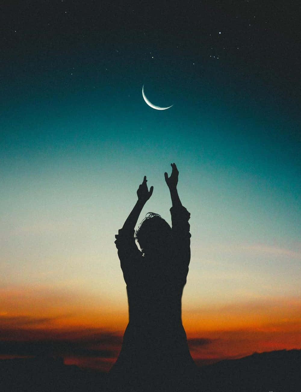 暮色中一個人向新月和星星伸出手的剪影。