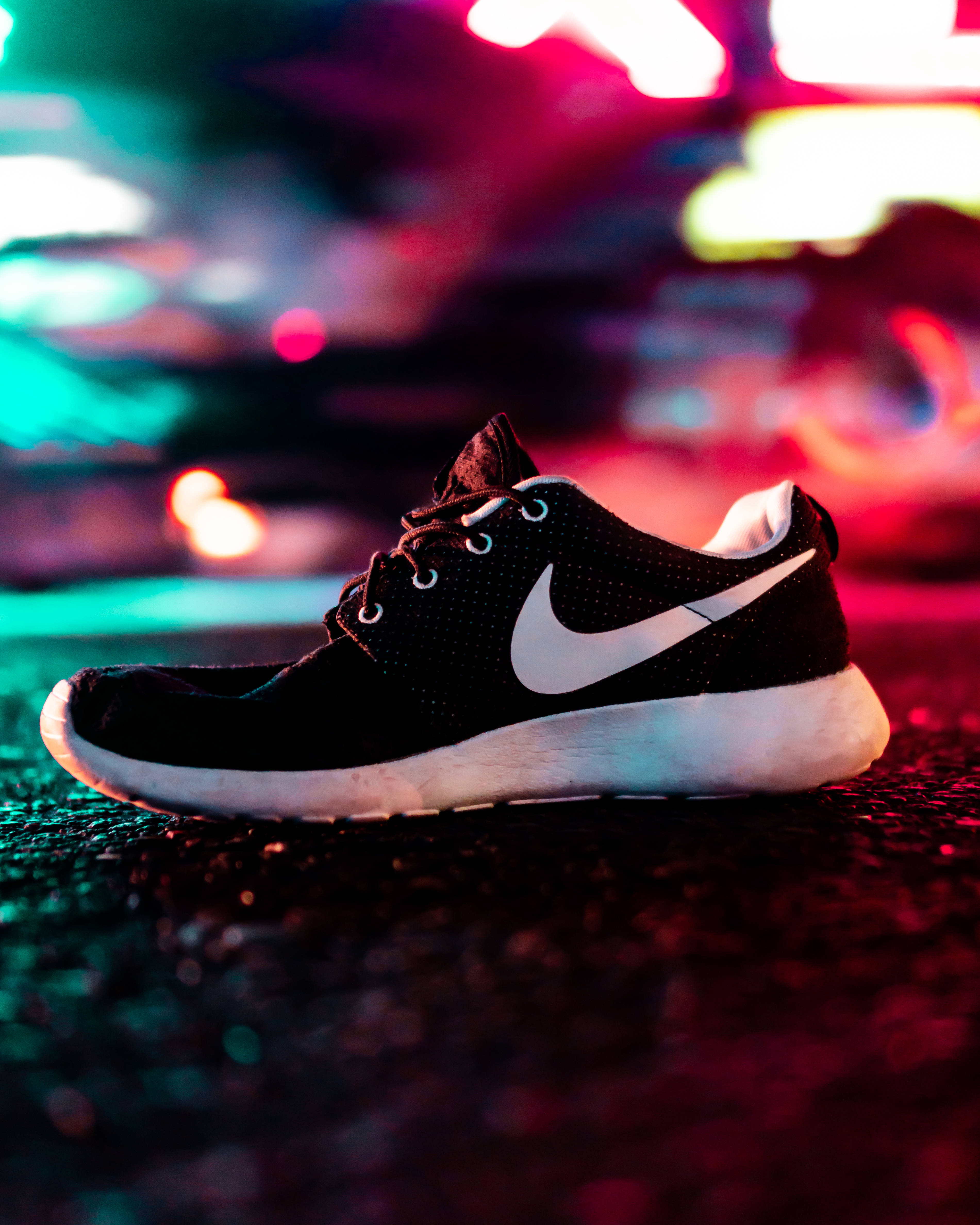 單隻黑白Nike運動鞋 壁紙 — 一雙帶有白色Swoosh的黑色Nike運動鞋在夜間濕漉漉的路面上，在充滿活力的霓虹燈光下休息。