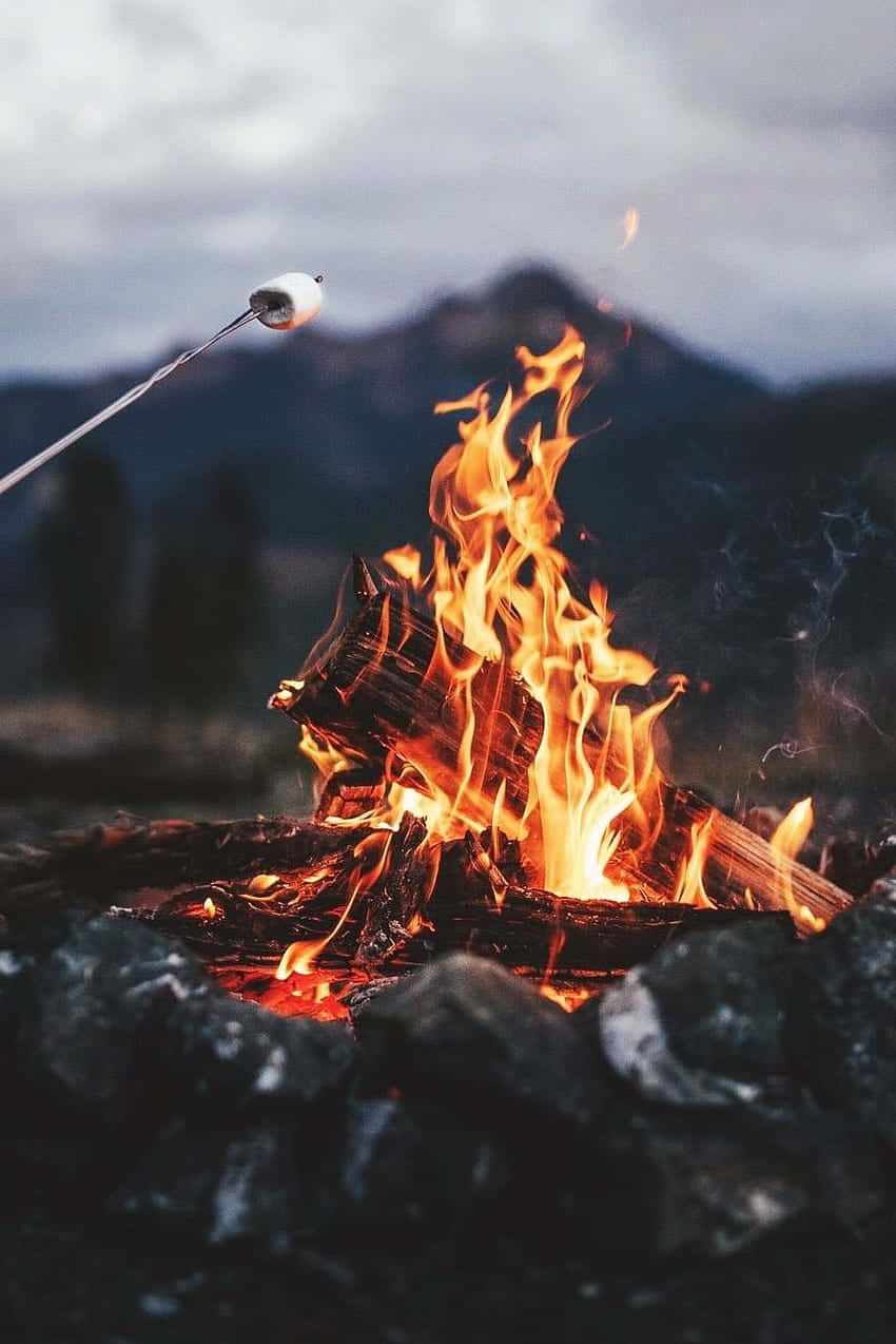 Fall Bonfire 桌布 壁紙 — 喺噼啪作響嘅營火上烤緊棉花糖，背景係煙霧繚繞嘅山脈。