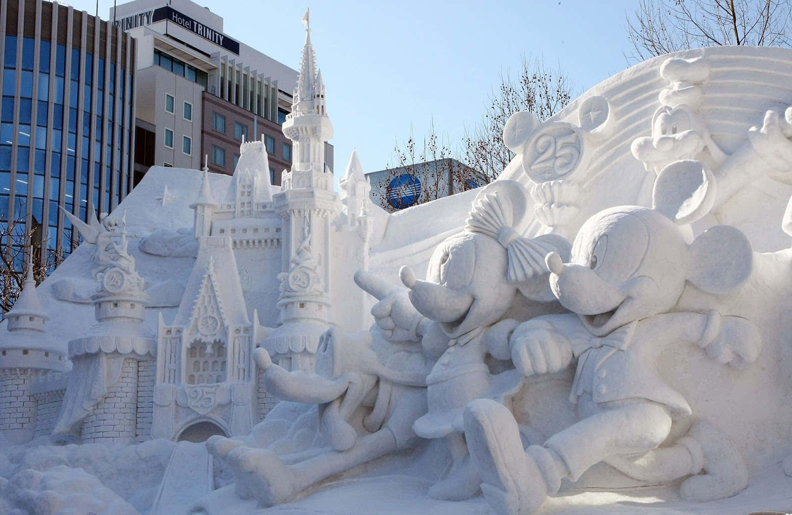Ice Sculpture 桌布 壁紙 — 喺晴朗藍天下，一個詳細嘅雪雕，展示米奇同米妮老鼠喺城堡旁邊，城堡上有 '25' 標誌。