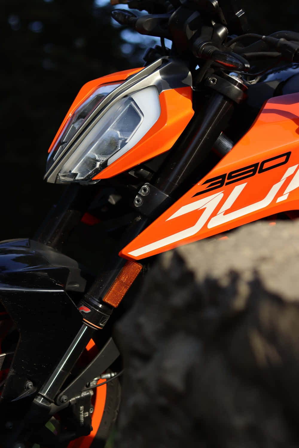 Duke 桌布 壁紙 — 喺模糊岩石地形背景下，鮮橙色KTM 390 Duke電單車頭燈同前整流罩嘅特寫。