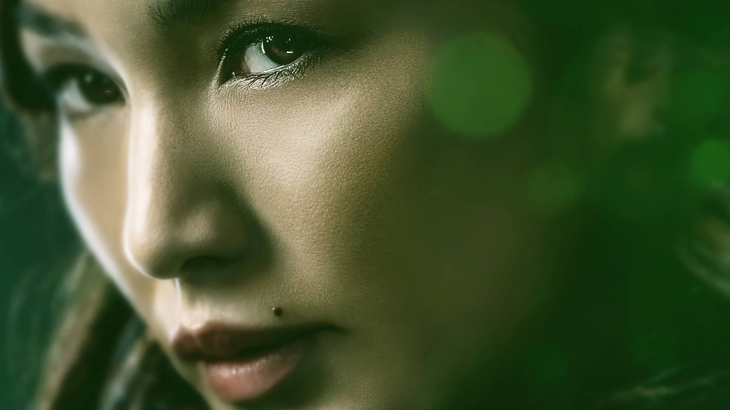 嘉瑪·陳《永恆族》 壁紙 — 一個女性臉部的特寫肖像，帶有柔和的綠色散景和溫暖的燈光，突顯她沉思的目光。