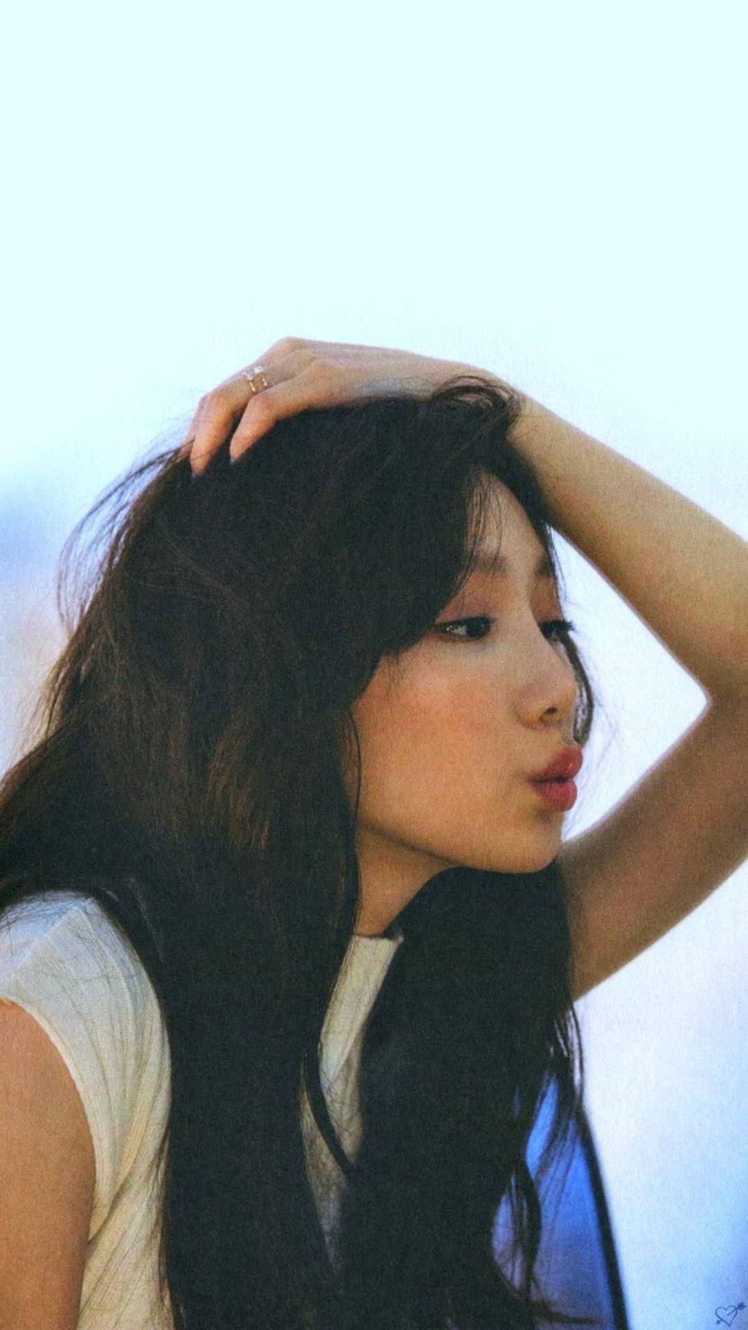 嘟嘴泰妍 壁紙 — 一位長黑髮的年輕女性輕輕地將頭靠在柔和的藍天背景上。