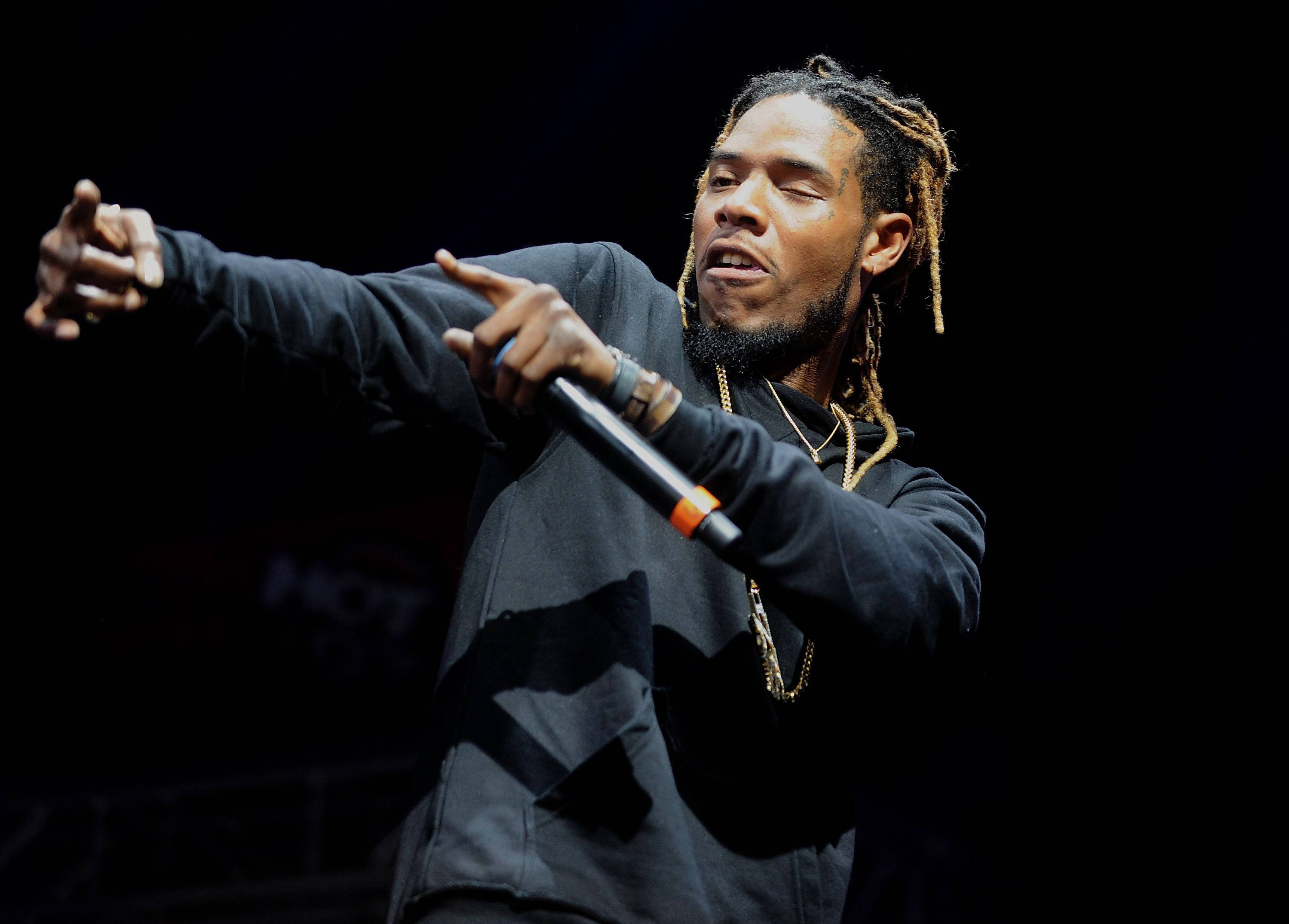 嘻哈藝術家Fetty Wap 壁紙 — 一位梳著辮子的饒舌歌手在戲劇性的聚光燈下，手持麥克風熱情地表演。