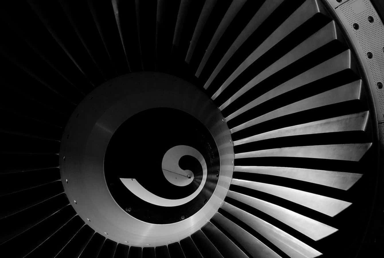 Jet Engine 桌布 壁紙 — 噴射引擎渦輪葉片從中央螺旋放射而出的單色特寫，強調工業幾何與金屬質感。