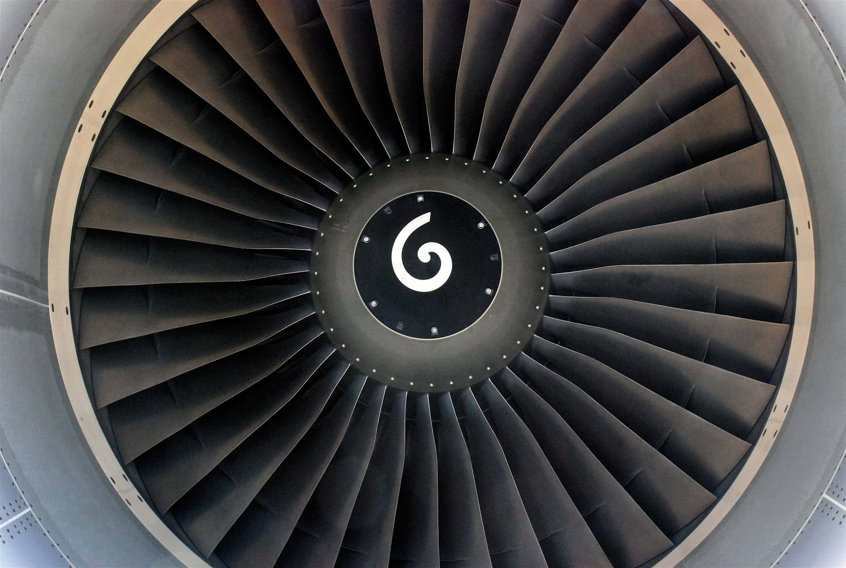 Jet Engine 桌布 壁紙 — 噴射引擎風扇葉片特寫，中央有旋渦標誌，背景為金屬灰和黑色色調。