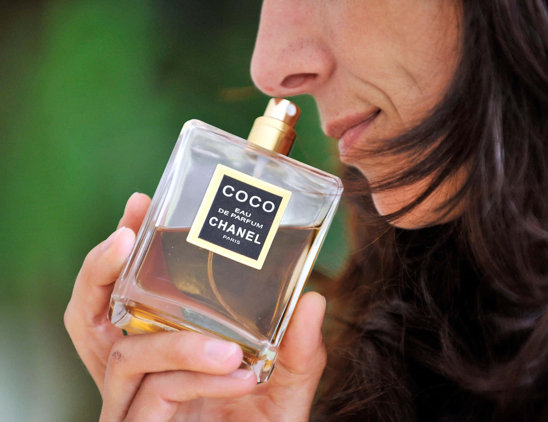 女士在柔和的綠色背景下聞Chanel Coco香水瓶。