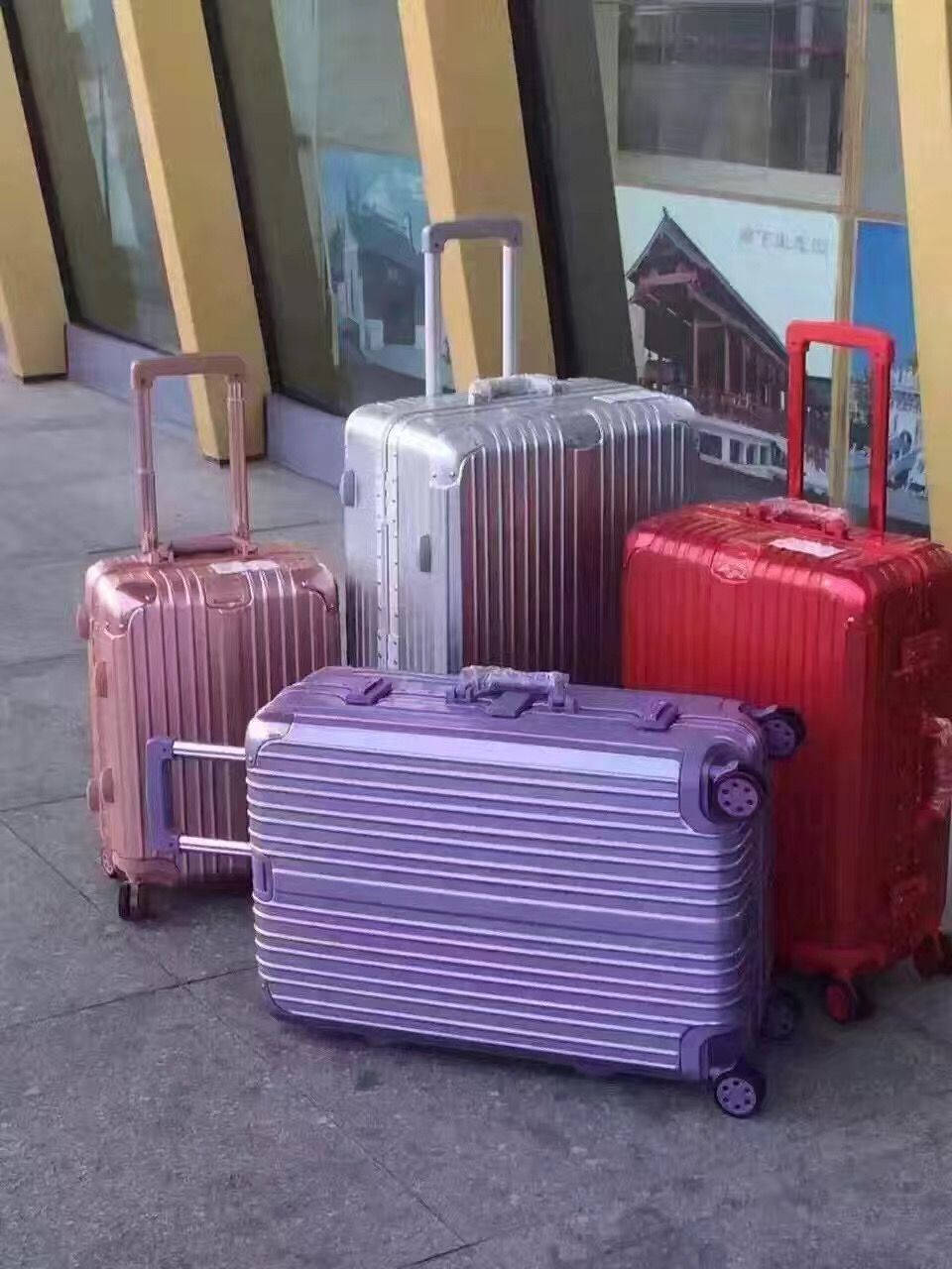 四個色彩繽紛的金屬行李箱放在行人路上，靠近一棟現代建築。