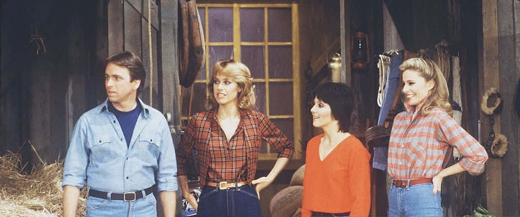 John Ritter 桌布 壁紙 — 四位1980年代演員站在質樸的木製穀倉門口，背景有乾草和懸掛的馬具。