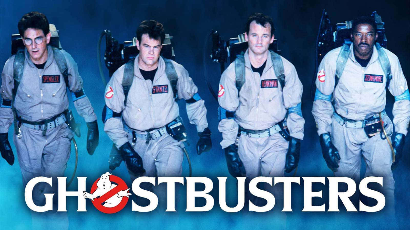 Ghostbusters 桌布 壁紙 — 四位捉鬼敢死隊身穿標誌性質子背包裝備，在煙霧藍色背景前邁步向前，下方有捉鬼敢死隊標誌。