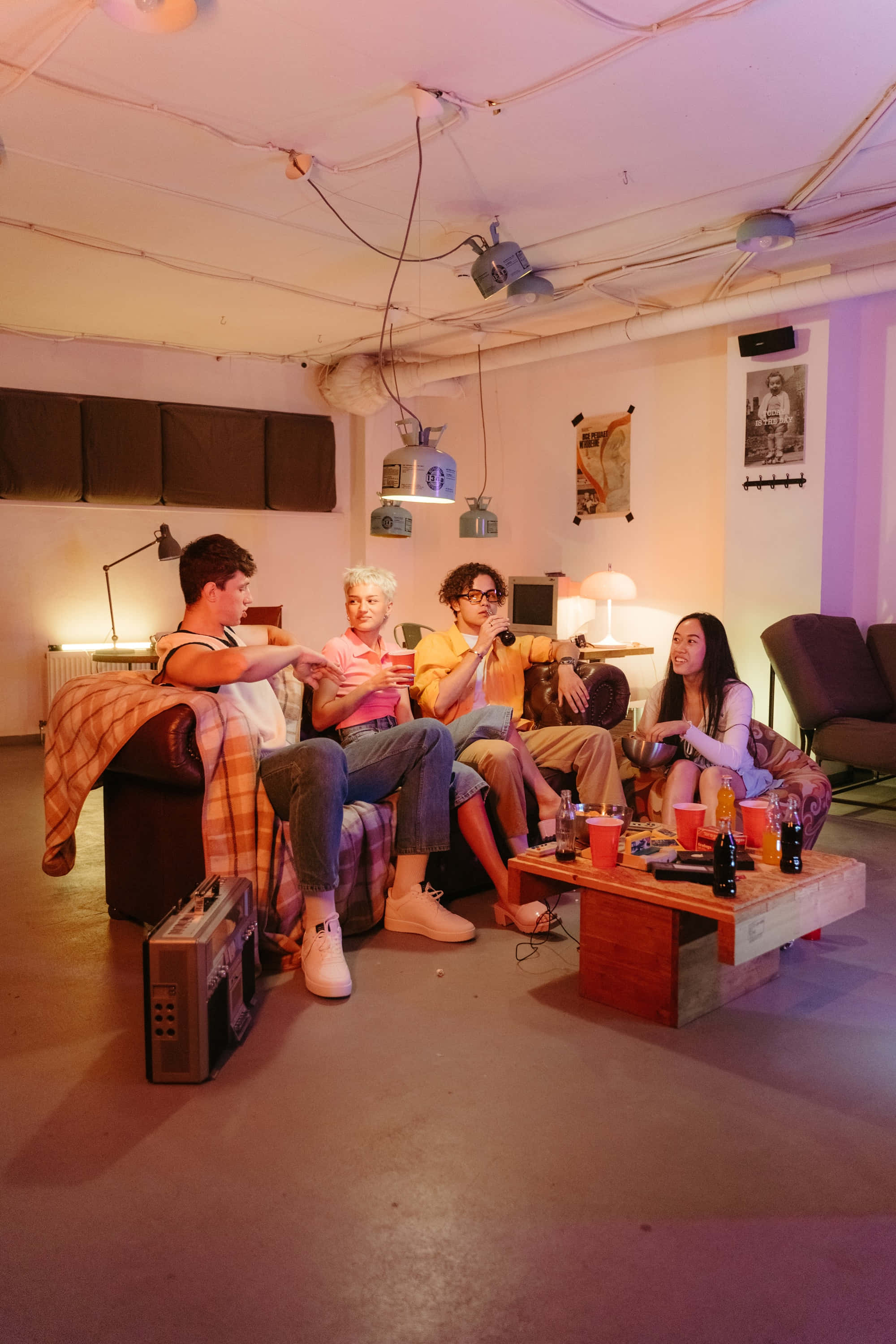 Youthful 桌布 壁紙 — 四位朋友在一個舒適、燈光溫暖、帶有裸露管道和復古裝飾的閣樓中笑著舉杯暢飲。