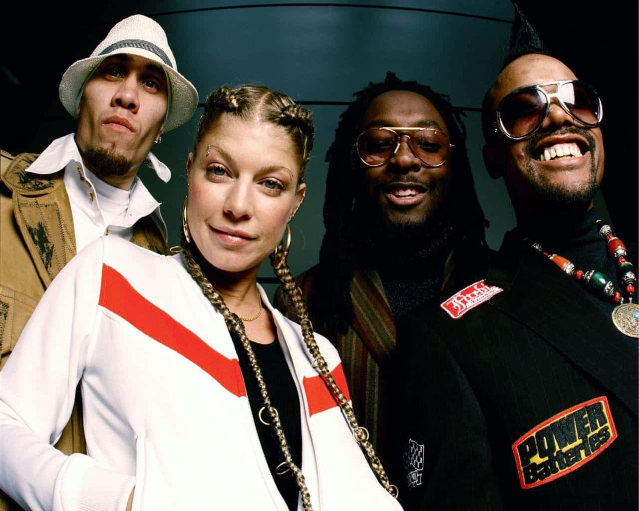 Black Eyed Peas 桌布 壁紙 — 四位穿著時尚的音樂人在深色弧形牆前自信地擺姿勢，展現大膽時尚和富有表現力的面孔。
